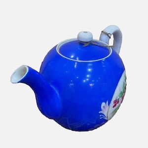 Könnte beinhalten: Eine blaue Teekanne aus Keramik mit einem weißen Deckel und einem Blumendesign an der Seite.