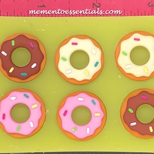 Könnte beinhalten: Eine Silikonform mit sechs Donut-Formen. Die Donuts sind in verschiedenen Farben, darunter Braun, Rosa und Weiß, und haben bunte Streusel.