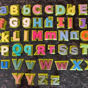 Peut inclure: Un ensemble de tampons en lettres de l'alphabet colorés, chaque lettre est dans un cadre vert. Les lettres sont en majuscules et en minuscules, et les couleurs sont vives et vibrantes.