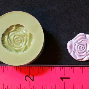 Könnte beinhalten: Eine grüne Silikonform mit Rosenmuster und eine weiße Rose, die aus der Form hergestellt wurde. Die Form und die Rose befinden sich neben einem Lineal mit Zollmarkierungen.