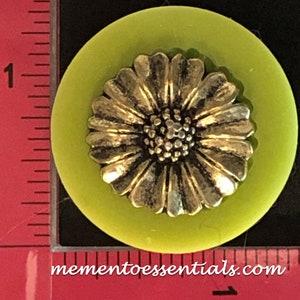 Könnte beinhalten: Ein limegrüner Knopf mit einem silbernen Gänseblümchen-Design. Der Knopf hat einen Durchmesser von etwa 2,5 cm.