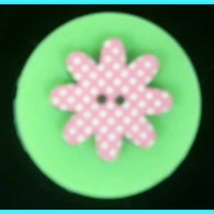 May include: A pink flower button with white polka dots on a green background.