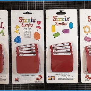 Könnte beinhalten: Vier Sizzix Sizzlits Stanzformen-Sets auf weißen Karten. Die Sets enthalten Buchstaben, Bienenmotive, Etiketten und Vintage-Designs. Jedes Set hat einen Stapel roter Stanzformen mit weißen Etiketten. Das Sizzix-Logo befindet sich oben.