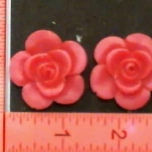 May include: Two pink plastic rose-shaped embellishments. The roses are approximately 2.5 cm in diameter.