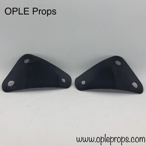 May include: Two black metal brackets with three holes each. The brackets are angled and have a smooth, matte finish. OPLE Props is printed in white at the top of the image. The website address www.opleprops.com is printed at the bottom of the image.