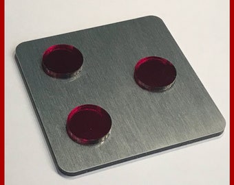 Może przedstawiać: Srebrna metalowa płytka z trzema czerwonymi okrągłymi wkładkami. Płytka ma nadrukowany tekst "MADE IN GERMANY" i "www.opleprops.com".