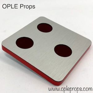 Könnte beinhalten: Ein quadratischer Untersetzer mit gebürsteter Metalloberfläche und drei dunkelroten kreisförmigen Einsätzen. Der Untersetzer hat einen roten Rand. Der Text "OPLE Props" und "www.opleprops.com" sind sichtbar.