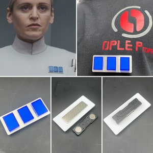 Könnte beinhalten: Drei blaue rechteckige Abzeichen mit silbernem Rand, horizontal auf einem silbernen Hintergrund angeordnet. Die Abzeichen befinden sich auf einer weißen Oberfläche. Der Text "CAUTION MAGNETIC" ist auf einem weißen Abzeichen mit einem roten Dreieckswarnsymbol sichtbar.