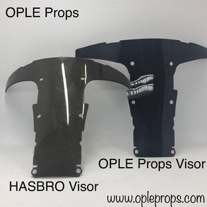 May include: Two motorcycle visors, one labeled "HASBRO Visor" and the other "OPLE Props Visor". Both visors are black and made of a clear plastic material. The visors are shown against a white background.