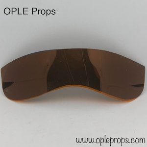 May include: A pair of brown, curved, plastic sunglasses. The sunglasses are reflective and have a slight sheen. The text "OPLE Props" is visible in the top left corner of the image. The text "www.opleprops.com" is visible in the bottom right corner of the image.