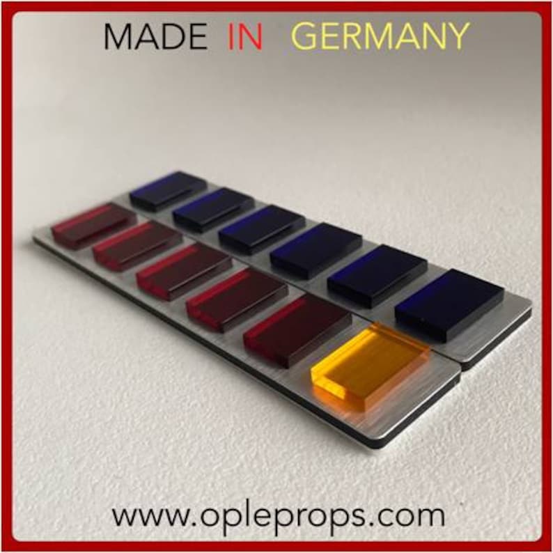 May include: A close-up of a silver panel with a row of colored buttons. The buttons are red, orange, yellow, green, blue, and purple. The panel is labeled "MADE IN GERMANY" and "www.opleprops.com".