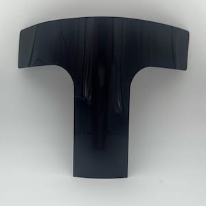 May include: A black plastic T-shaped piece with a curved top and a straight bottom.