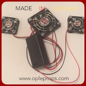 May include: Three small black computer fans with silver wire mesh grills and red and black wires connected to a black battery pack. The fans are labeled "MADE IN GERMANY" and the battery pack has the website "www.opleprops.com" printed on it.