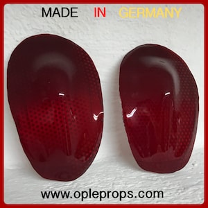 Puede incluir: Dos cubiertas de luces traseras de coche de plástico rojo con un patrón de puntos. Las cubiertas están hechas en Alemania. El texto "www.opleprops.com" está impreso debajo de las cubiertas.