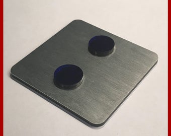 May include: A silver metal square with two black round buttons. The square has the text "MADE IN GERMANY" and "www.opleprops.com" printed on it.