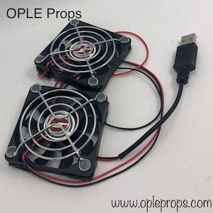 May include: Two black computer cooling fans with silver wire mesh grills and a USB connector. The fans are connected by wires and have adhesive backing. The text "OPLE Props" is visible in the top left corner of the image. The text "www.opleprops.com" is visible in the bottom right corner of the image.
