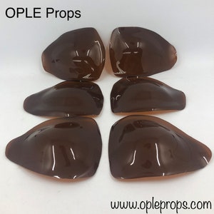 Puede incluir: Seis accesorios marrones, brillantes y curvos están dispuestos en un patrón circular. Los accesorios tienen una superficie lisa y reflectante. El texto "OPLE Props" está en la parte superior y "www.opleprops.com" en la inferior.