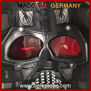 May include: Close-up of a black Darth Vader helmet with red tinted lenses. The helmet has a textured surface and the text "MADE IN GERMANY" and "www.copleprops.com" are visible.