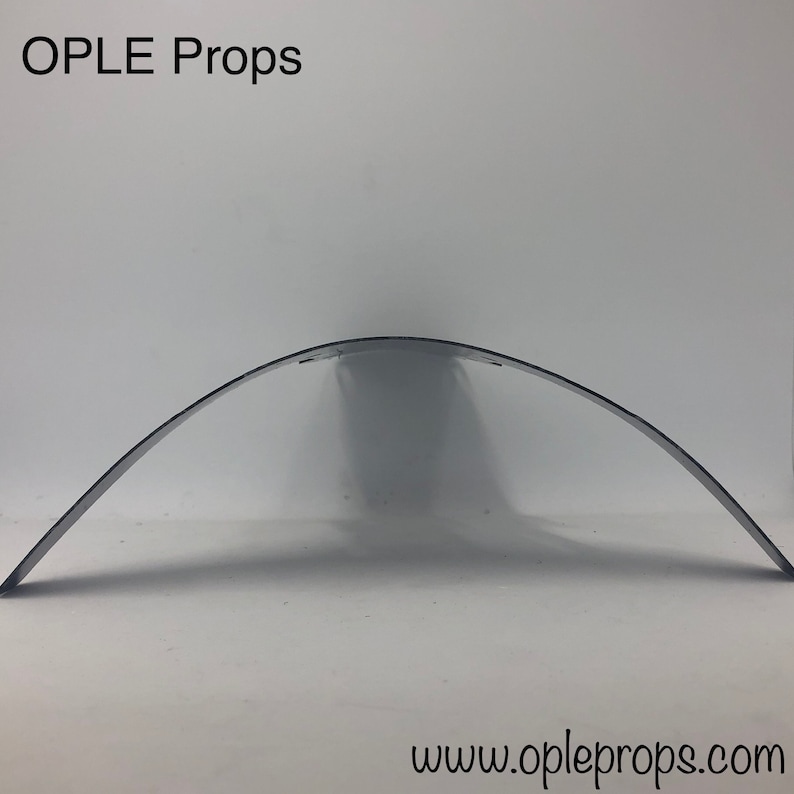 May include: A silver metal archway prop, curved and slightly bent, for use in photography or film sets. The archway is made of a single piece of metal and is designed to be lightweight and easy to move.
