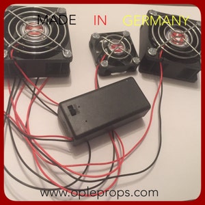 May include: Three black computer fans with a black battery pack and red and black wires. The fans are labeled "MADE IN GERMANY". The website "www.oppleprops.com" is printed on the white surface.
