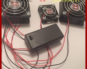 May include: Three black computer fans with a black battery pack and red and black wires. The fans are labeled "MADE IN GERMANY". The website "www.oppleprops.com" is printed on the white surface.
