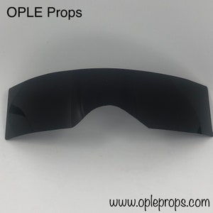 May include: Black plastic visor for a costume or prop. The visor is curved and has a slight arch in the centre. The text "OPLE Props" is visible at the top of the image.