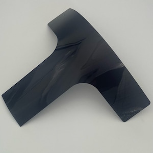 Puede incluir: Una pieza de plástico negra en forma de T con un acabado liso y brillante.