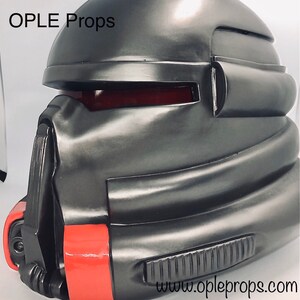 May include: A black helmet with red accents and a textured surface. The helmet has a visor and a chin guard. The text "OPLE Props" and "www.opleprops.com" are visible on the helmet.