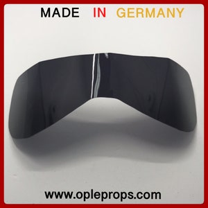 May include: Black plastic visor for a motorcycle helmet. The visor is curved and has a slight tint. The text "MADE IN GERMANY" is printed on the top of the image. The text "www.opleprops.com" is printed on the bottom of the image.