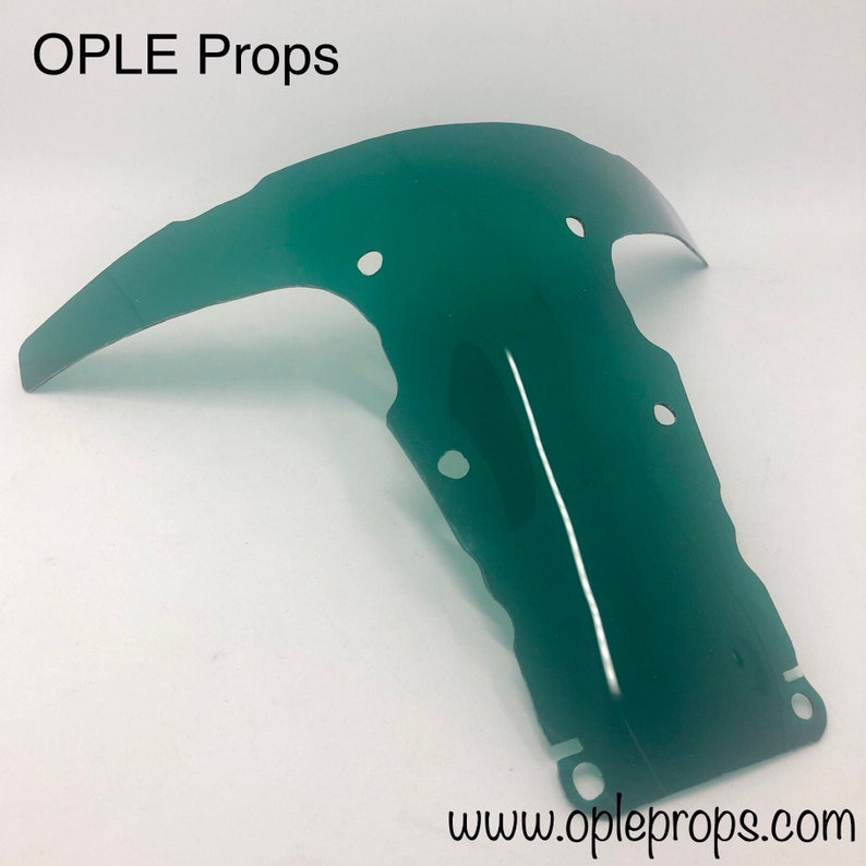 May include: A green plastic prop for a movie or play. The prop is shaped like a curved, open-ended tube with several holes. The prop is made of a translucent material and has a slight sheen.