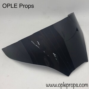May include: A black plastic visor for a motorcycle helmet. The visor is curved and has a slight tint. The visor is made by OPLE Props.