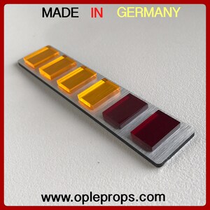 Puede incluir: Una barra de metal plateado con siete luces rectangulares. Las luces est&aacute;n dispuestas en fila y son amarillas y rojas. La barra tiene el texto "MADE IN GERMANY" impreso en ella. La barra tambi&eacute;n tiene el texto "www.opleprops.com" impreso en ella.