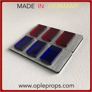 Op de afbeelding: Een rechthoekig, zilverkleurig Starfleet-commandobadge met vijf rode en vijf blauwe rechthoekige lampjes. Het badge is gemaakt van plastic en heeft een geborstelde metalen afwerking. De tekst "MADE IN GERMANY" is bovenaan de afbeelding gedrukt. De tekst "www.opleprops.com" is onderaan de afbeelding gedrukt.
