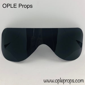 Puede incluir: Un par de gafas de sol de plástico negro con una forma única y curvada. Las gafas de sol están hechas de un material liso y brillante.