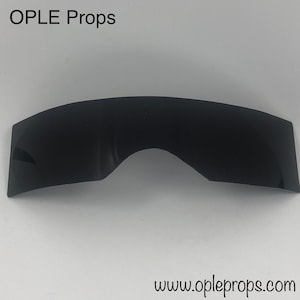 May include: Black plastic visor for a costume or prop. The visor is curved and has a slight arch in the center. The text "OPLE Props" is visible at the top of the image.