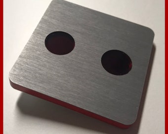 May include: A square, brushed metal plate with two circular holes. The edges are red, and the surface has a linear grain. The text "MADE IN GERMANY" is at the top. The website address www.opleprops.com is at the bottom.