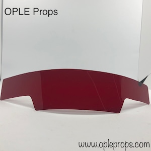May include: A curved, red plastic visor with a slight bend in the middle. The visor is made of a clear plastic material and has a slight sheen. The text "OPLE Props" is visible in the top left corner of the image. The text "www.opleprops.com" is visible in the bottom right corner of the image.