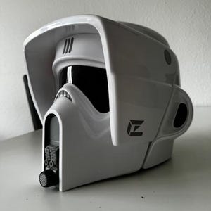 Può includere: Un casco bianco con una visiera nera e un logo 'Z' grigio. Il casco ha una superficie testurizzata e un piccolo altoparlante nero rotondo sul lato.