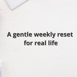 May include: White textured surface with the text "A gentle weekly reset for real life." A small succulent plant in a gray pot, a gold geometric object, and a white notebook are visible.