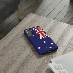 May include: A blue phone case featuring the Australian flag printed on it. The case has a black camera cutout and a black border.