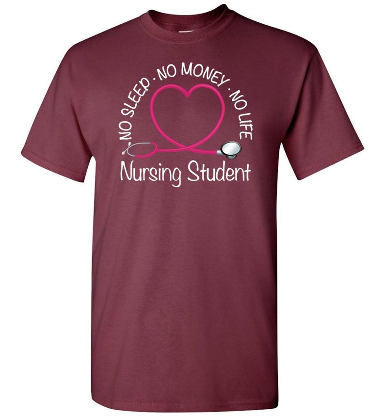 Peut inclure: T-shirt bordeaux avec un motif de st&eacute;thoscope rose en forme de c&oelig;ur. Le texte indique "NO SLEEP - NO MONEY - NO LIFE" et "Nursing Student" en blanc. Un v&ecirc;tement d&eacute;contract&eacute; pour les &eacute;tudiants en soins infirmiers.
