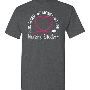 Peut inclure: T-shirt gris fonc&eacute; avec un motif de st&eacute;thoscope rose en forme de c&oelig;ur. Le texte indique "NO SLEEP - NO MONEY - NO LIFE" autour du c&oelig;ur, avec "Nursing Student" en dessous. Un t-shirt d&eacute;contract&eacute; pour &eacute;tudiants.