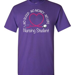Peut inclure: T-shirt violet avec un motif blanc. Le motif comprend le texte "NO SLEEP - NO MONEY - NO LIFE" autour d'un st&eacute;thoscope rose en forme de c&oelig;ur. Le texte "Nursing Student" est en dessous.