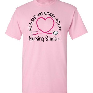Peut inclure: T-shirt rose clair avec un motif pour &eacute;tudiants en soins infirmiers. Le motif comprend un st&eacute;thoscope rose en forme de c&oelig;ur, avec les mots "NO SLEEP, NO MONEY, NO LIFE" au-dessus du c&oelig;ur et "Nursing Student" en dessous.