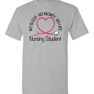 Peut inclure: T-shirt gris clair avec un motif de st&eacute;thoscope rose en forme de c&oelig;ur. Le texte autour du c&oelig;ur indique &laquo;&nbsp;NO SLEEP - NO MONEY - NO LIFE&nbsp;&raquo; et &laquo;&nbsp;Nursing Student&nbsp;&raquo; est imprim&eacute; en dessous.