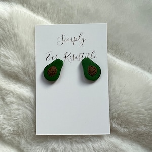 May include: A pair of avocado-shaped earrings with brown seeds. The earrings are on a white card with the text "Simply Ear-Resistible".