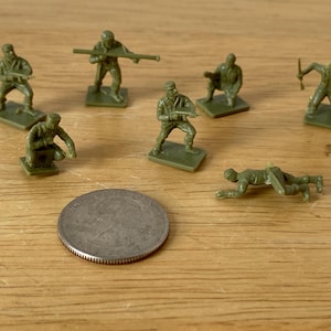 May include: A set of seven green plastic toy soldiers in various poses. The soldiers are holding weapons and are standing on small bases.