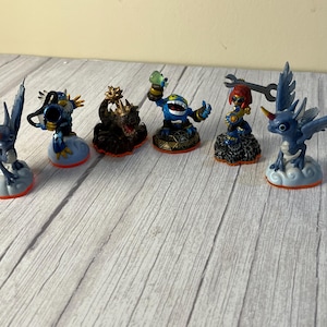 May include: Six blue and silver Skylanders figures with wings, standing on cloud-shaped bases. The figures are from the Skylanders video game series.
