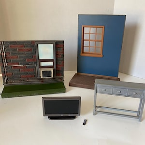 May include: Miniature dollhouse furniture and architectural elements. Includes a small TV, a gray console table with three drawers, and two wall sections with windows. A remote control is also present.