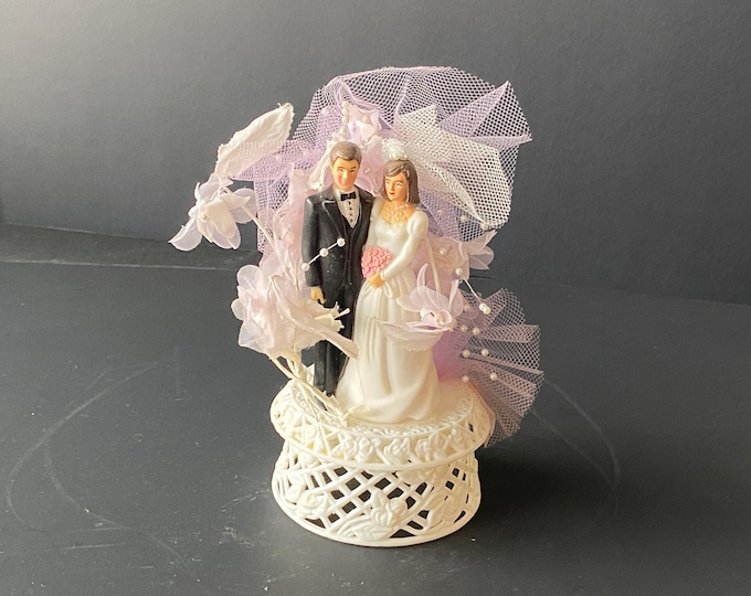 1986 Plastic Bride and Groom Cake Topper surrounded with a light Lavender tulle and silk type flowers with sprays of pearls